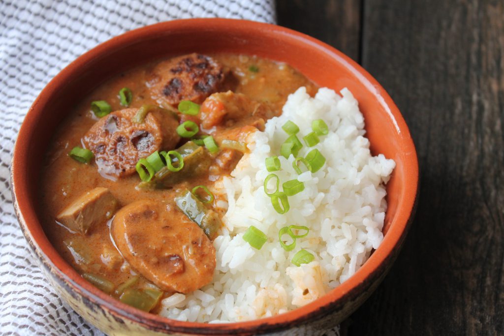 A bowl filled with vegan sausage and chicken gumbo served over a bed of fluffy white rice, garnished with chopped green onions.