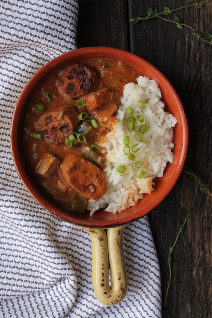 A bowl filled with vegan sausage and chicken gumbo served over a bed of fluffy white rice, garnished with chopped green onions.