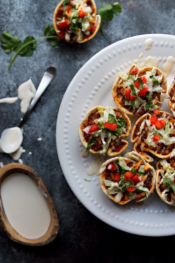 Close-up of crispy vegan taco cups filled with seasoned meat, vegan cheese, and fresh toppings.
