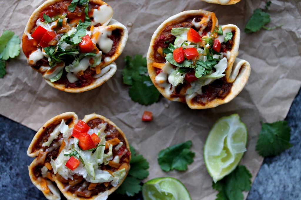 Close-up of crispy vegan taco cups filled with seasoned meat, vegan cheese, and fresh toppings.