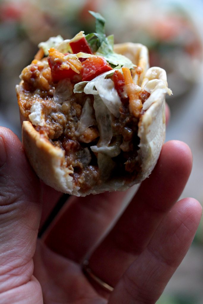 Close-up of crispy vegan taco cups filled with seasoned meat, vegan cheese, and fresh toppings.
