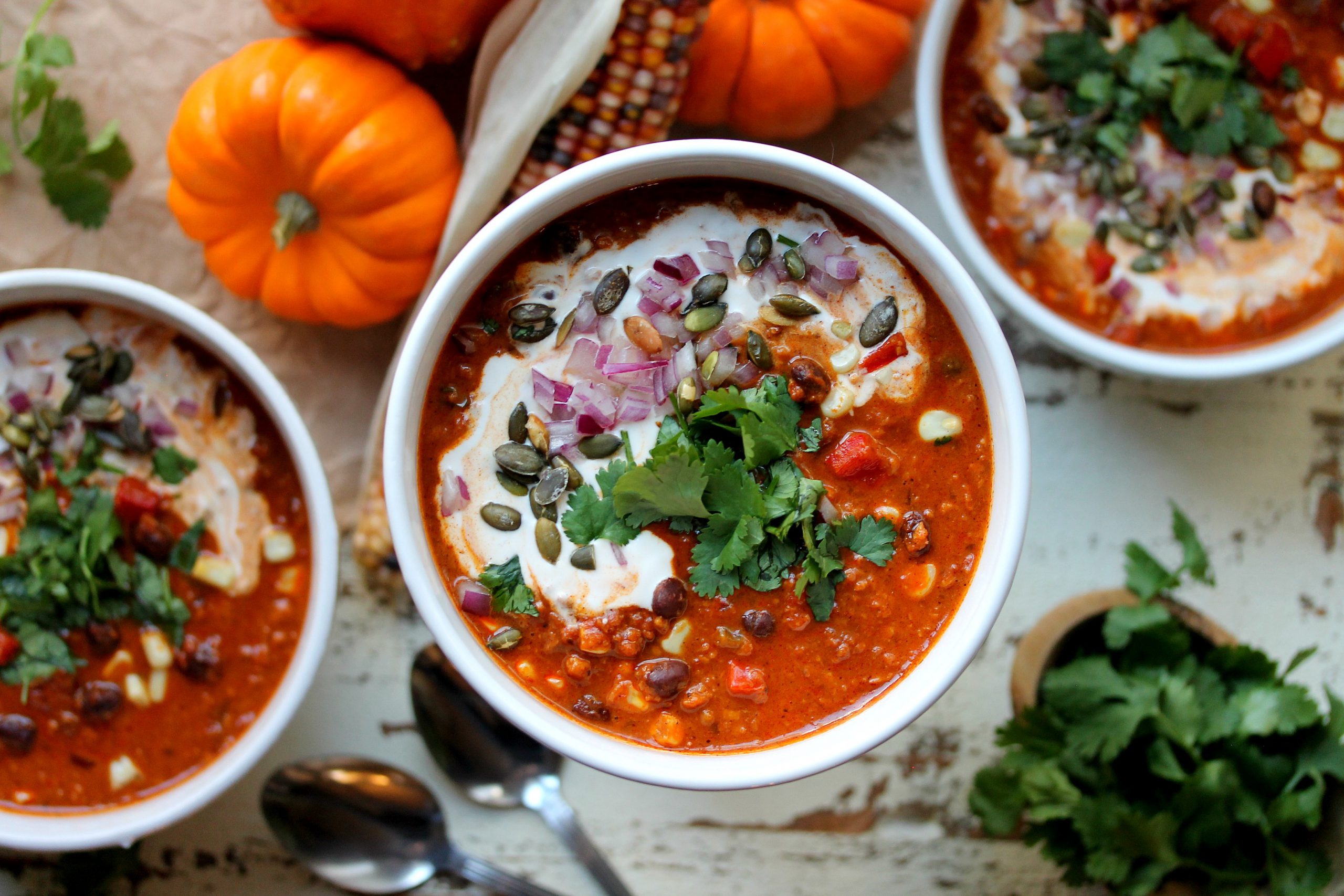 A hearty bowl of vegan soy chorizo and pumpkin chili topped with vegan sour cream, chopped cilantro, red onion, and seasoned pumpkin seeds.