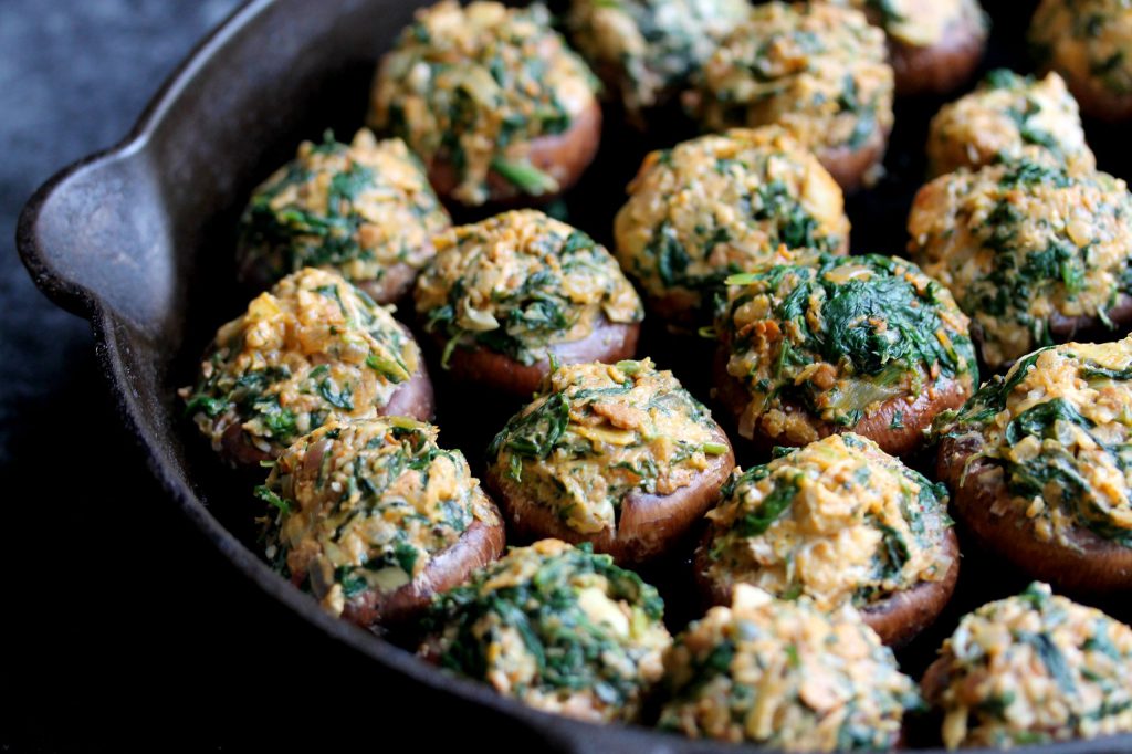 Mushroom caps stuffed with chorizo, spinach, and artichoke filling, topped with breadcrumbs, arranged on a baking sheet ready to go into the oven.
