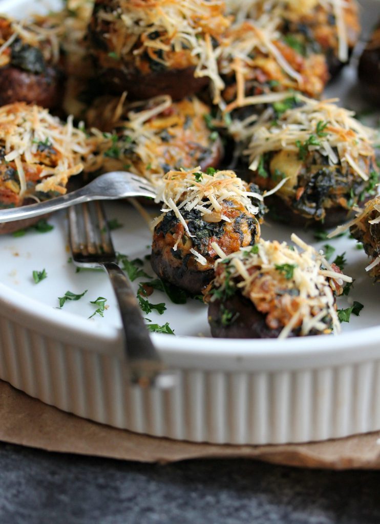Golden brown chorizo, spinach, and artichoke stuffed mushrooms garnished with fresh parsley, served on a white platter.