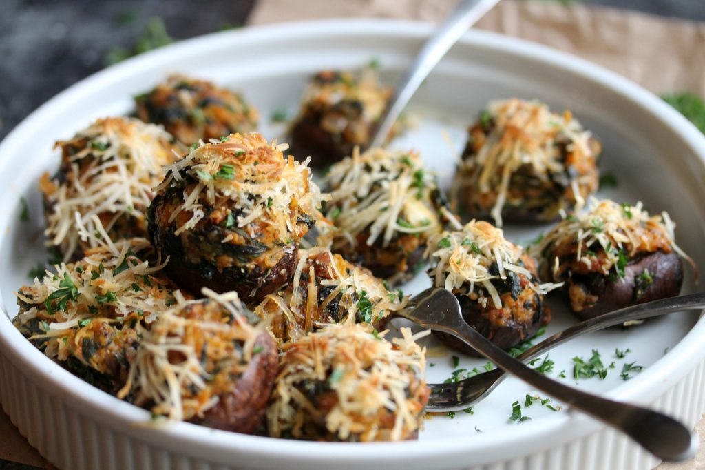 Golden brown chorizo, spinach, and artichoke stuffed mushrooms garnished with fresh parsley, served on a white platter.