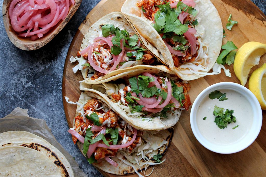 Assembled chipotle maple cauliflower tacos with shredded cabbage, cauliflower, pickled onions, lemon cream and cilantro.