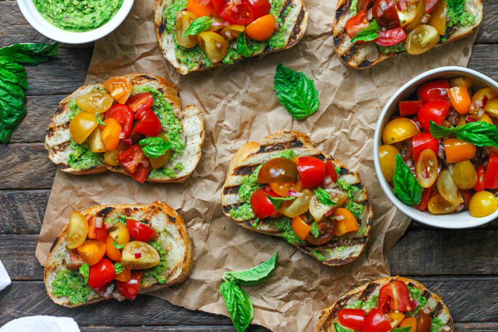 Vibrant vegan pea pesto bruschetta with tomato topping and fresh basil.