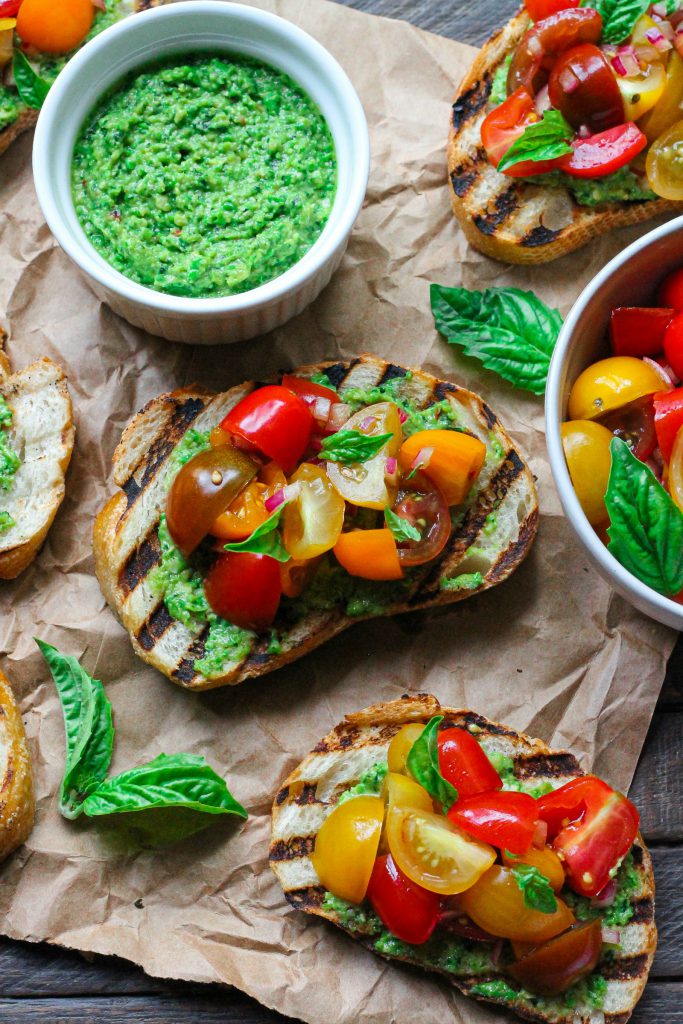 Vibrant vegan pea pesto bruschetta with tomato topping and fresh basil.