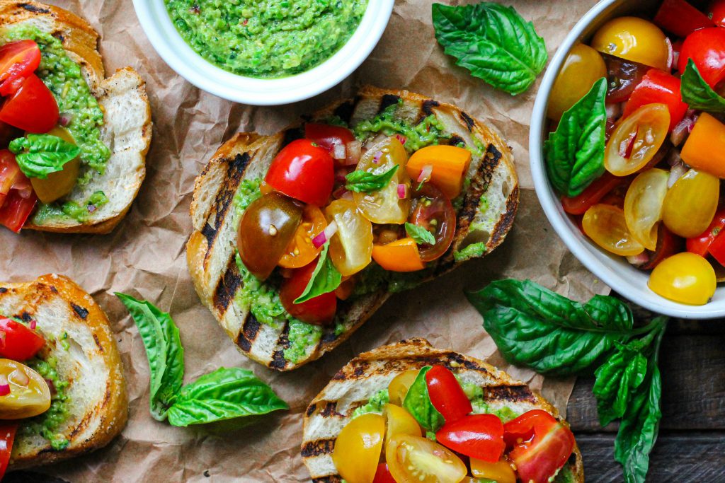 Vibrant vegan pea pesto bruschetta with tomato topping and fresh basil.