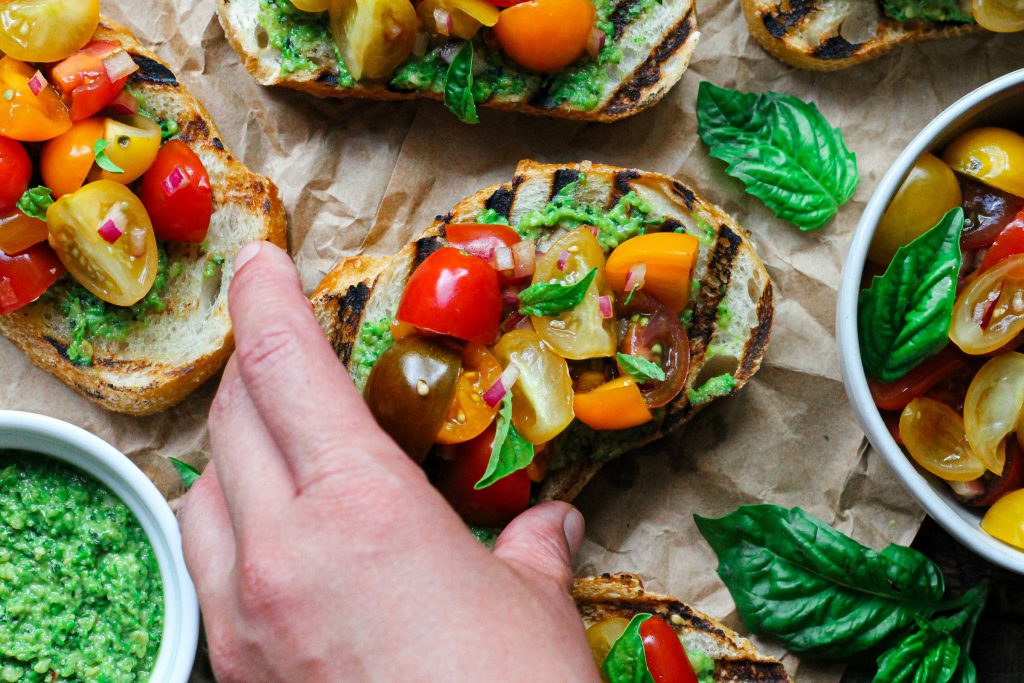 Vibrant vegan pea pesto bruschetta with tomato topping and fresh basil.