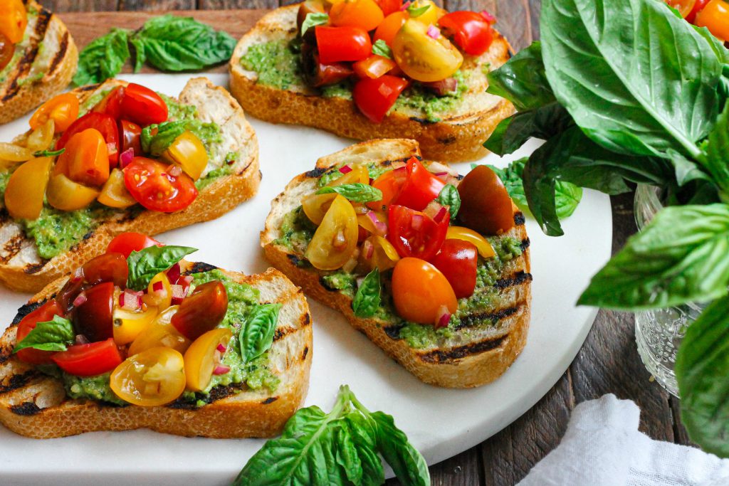 Vibrant vegan pea pesto bruschetta with tomato topping and fresh basil.