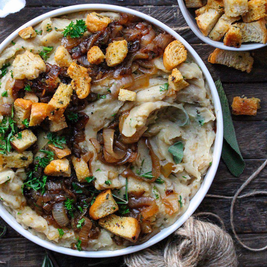 A bowl of creamy vegan French onion mashed potatoes topped with caramelized onions and crispy herby croutons.