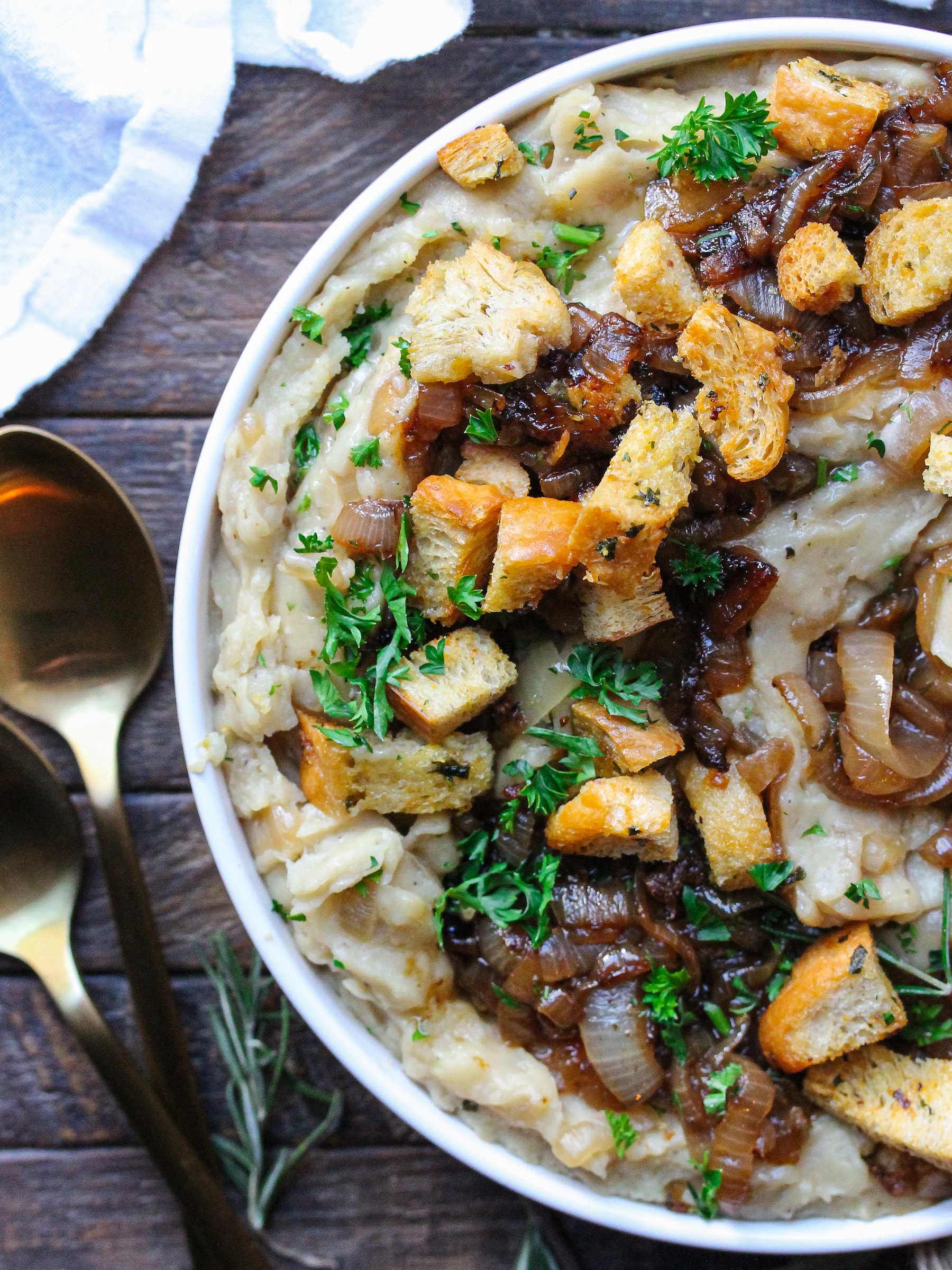 A bowl of creamy vegan French onion mashed potatoes topped with caramelized onions and crispy herby croutons.