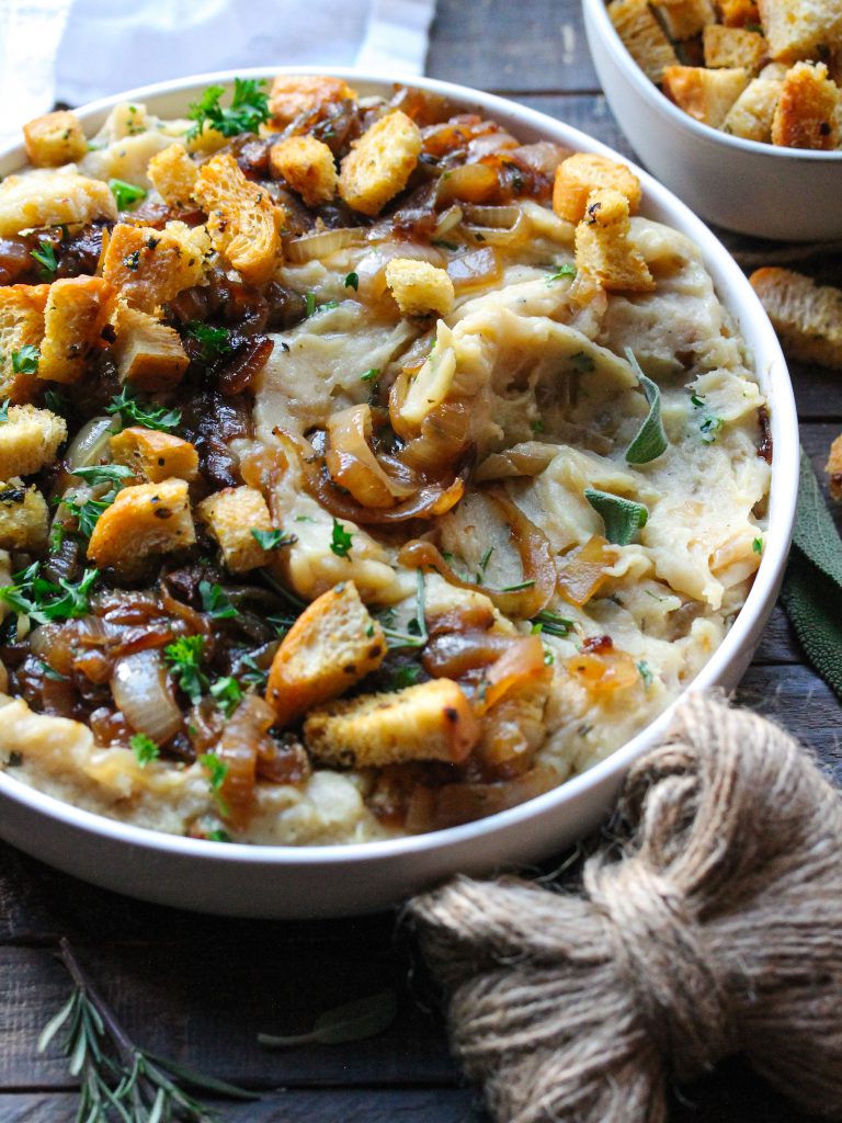 A bowl of creamy vegan French onion mashed potatoes topped with caramelized onions and crispy herby croutons.