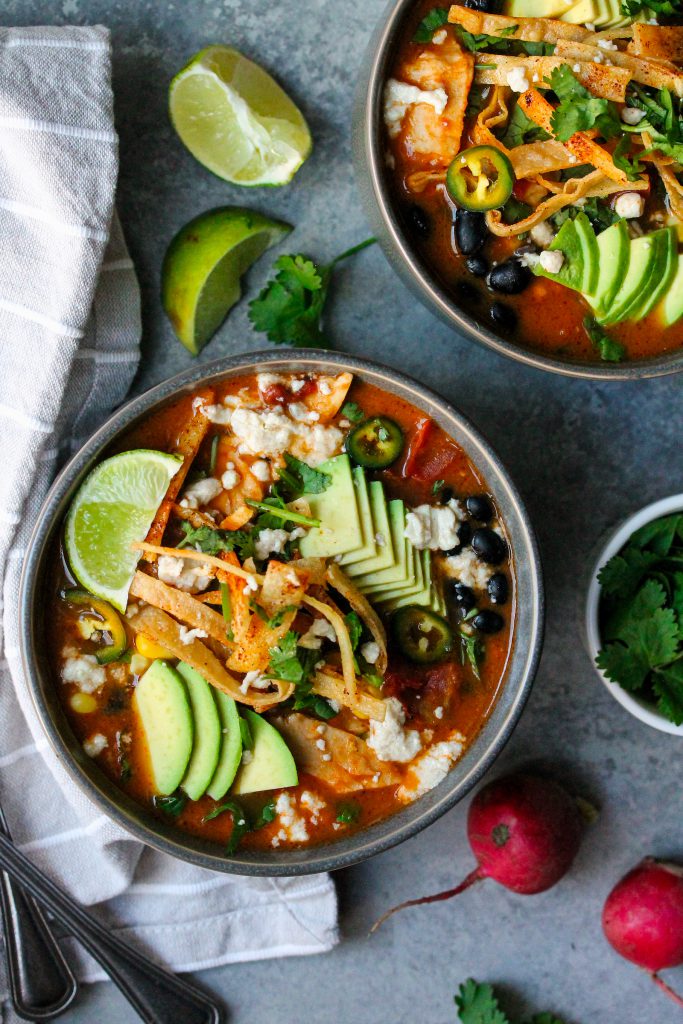 Bowl of hearty vegan tortilla soup garnished with crispy tortilla strips, sliced avocado, fresh cilantro, and a lime wedge.