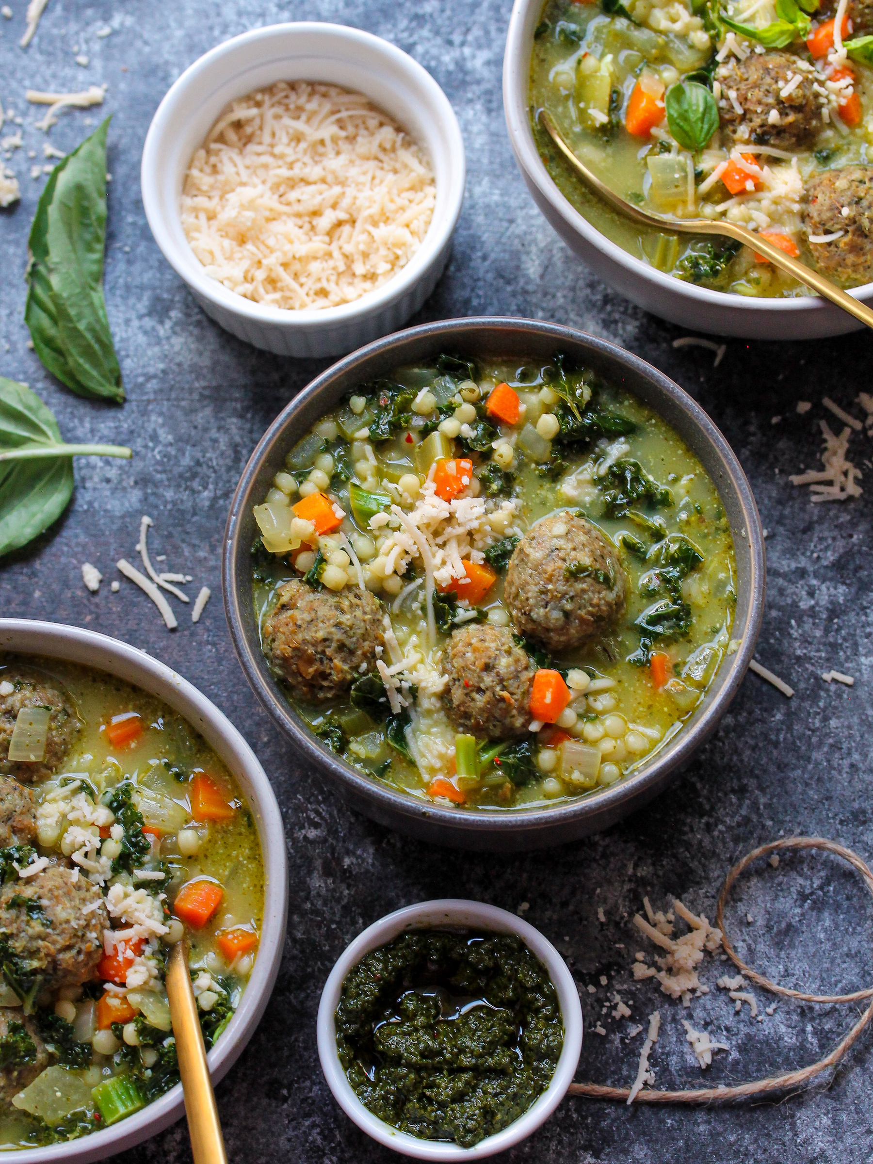 A close-up of a bowl of Pesto Italian Wedding Soup topped with vegan meatballs, kale, and julienned basil.