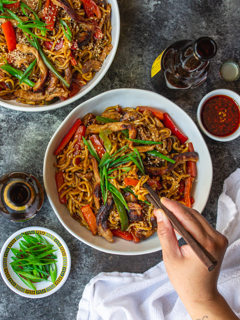 colorful and appetizing plate of peppered 'beef' stir-fried noodles topped with sliced green onions and toasted sesame seeds, ready to be enjoyed.
