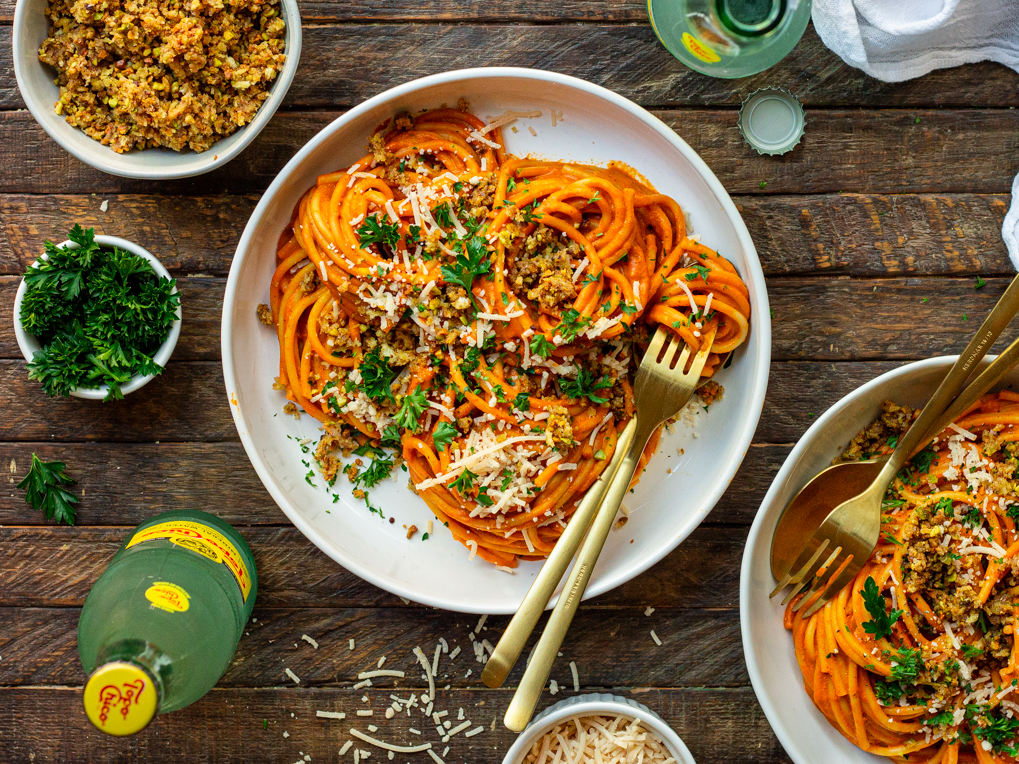 Bowl of creamy roasted red pepper pasta garnished with cheesy pistachio breadcrumbs and fresh parsley.