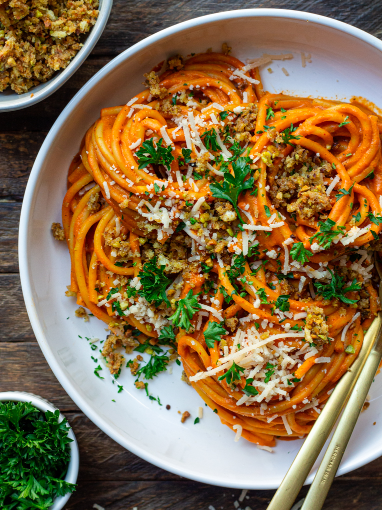 Bowl of creamy roasted red pepper pasta garnished with cheesy pistachio breadcrumbs and fresh parsley.