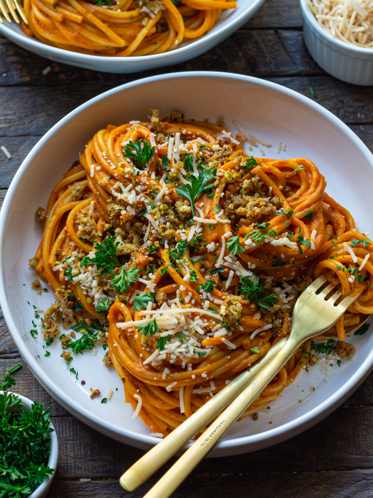 Bowl of creamy roasted red pepper pasta garnished with cheesy pistachio breadcrumbs and fresh parsley.