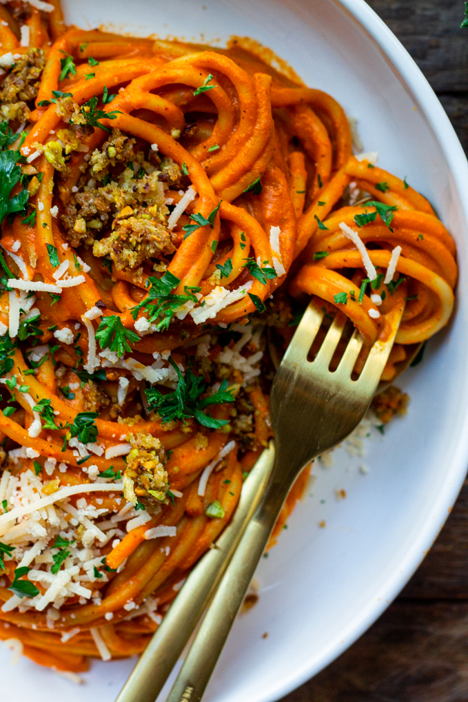 Bowl of creamy roasted red pepper pasta garnished with cheesy pistachio breadcrumbs and fresh parsley.
