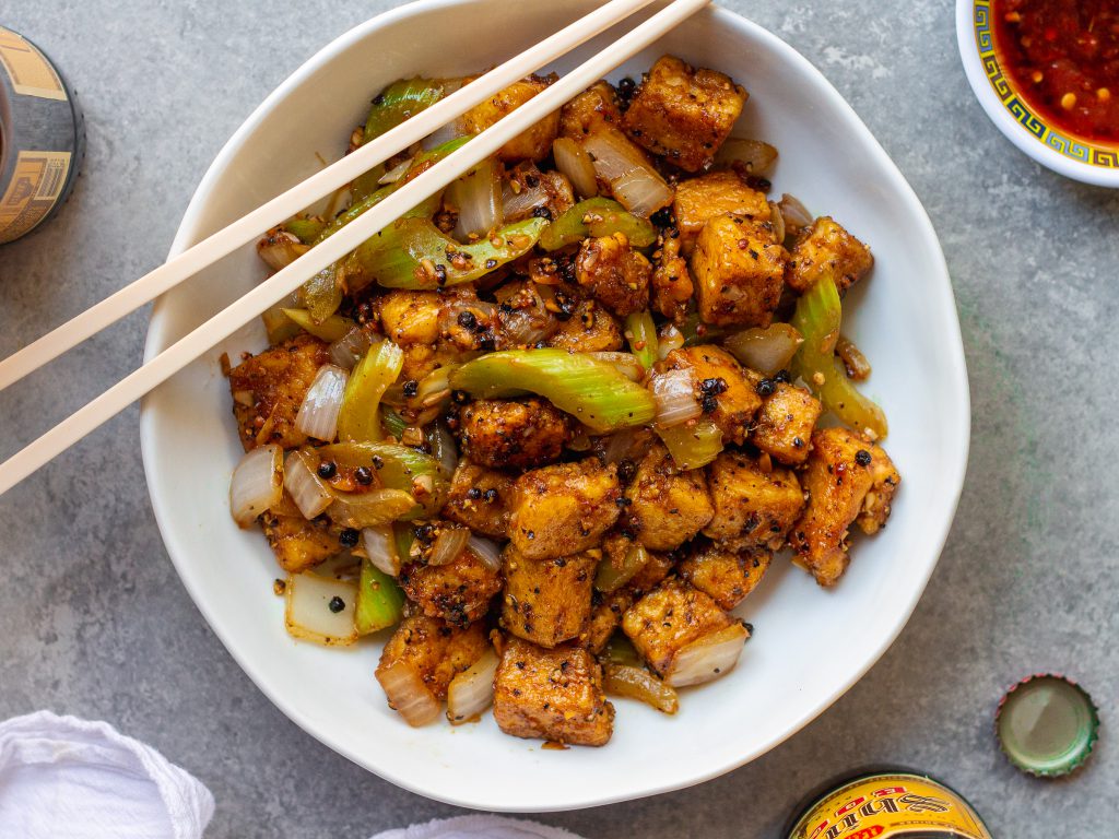 Close-up of crispy black pepper tofu with sautéed onion and crisp celery tossed in a glossy sauce.