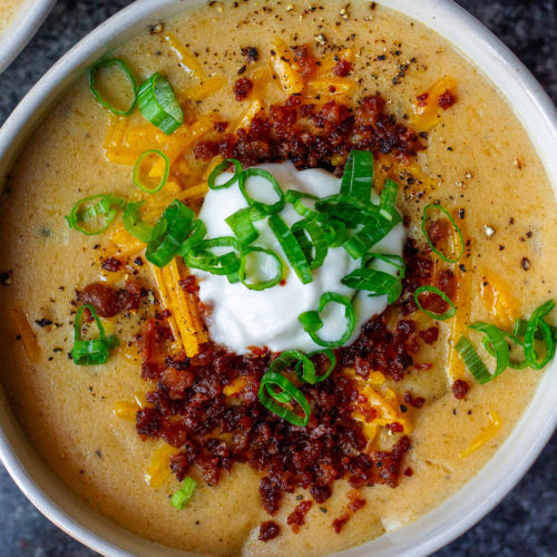 Bowl of vegan loaded baked potato soup topped with smoky tofu bacon, cheddar cheese, and chives.