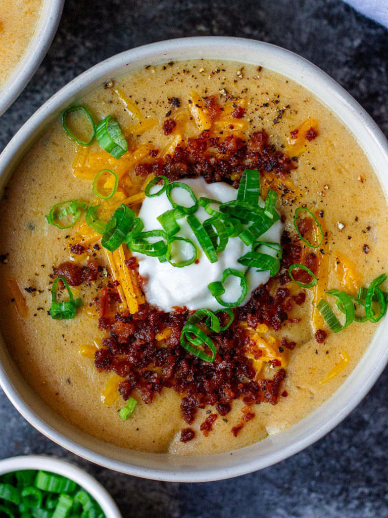 Bowl of vegan loaded baked potato soup topped with smoky tofu bacon, cheddar cheese, and chives.