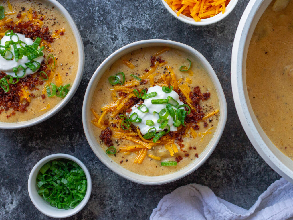 Bowl of vegan loaded baked potato soup topped with smoky tofu bacon, cheddar cheese, and chives.