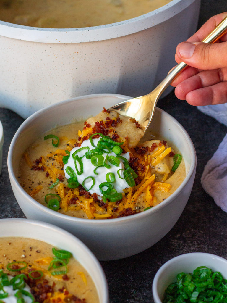 Bowl of vegan loaded baked potato soup topped with smoky tofu bacon, cheddar cheese, and chives.