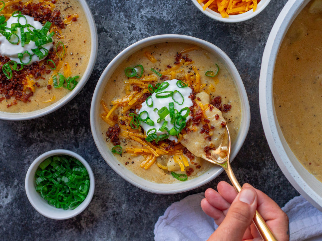 Bowl of vegan loaded baked potato soup topped with smoky tofu bacon, cheddar cheese, and chives.