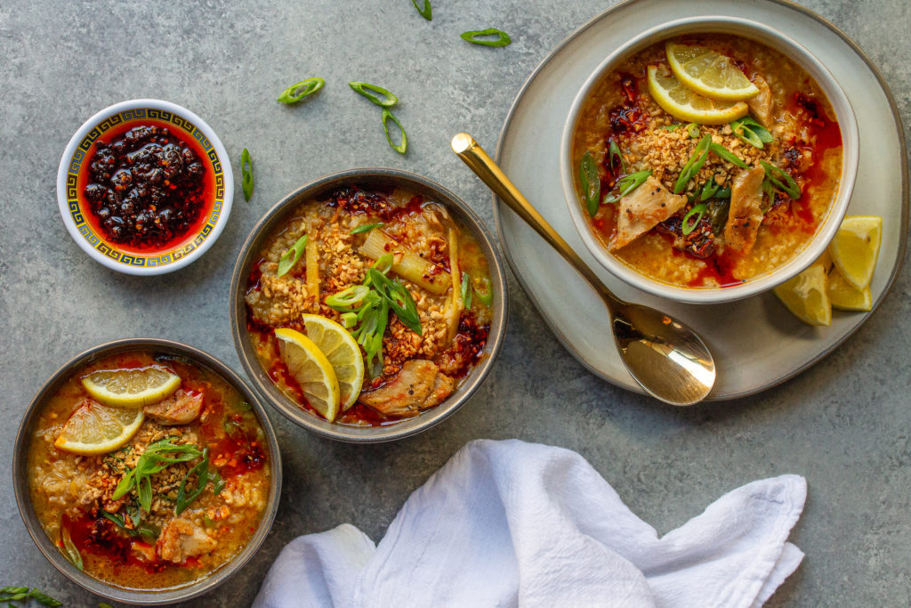 Bowl of creamy and comforting vegan arroz caldo garnished with chili oil, fried garlic, green onions, and lemon wedges.