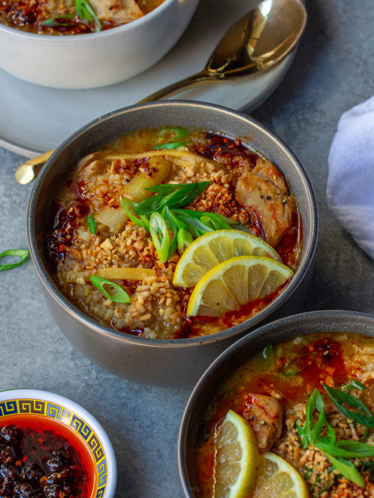 Bowl of creamy and comforting vegan arroz caldo garnished with chili oil, fried garlic, green onions, and lemon wedges.