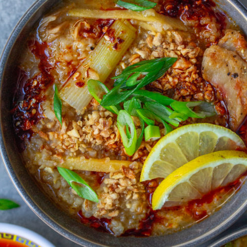 Bowl of creamy and comforting vegan arroz caldo garnished with chili oil, fried garlic, green onions, and lemon wedges.