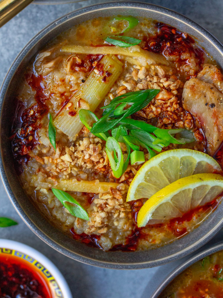 Bowl of creamy and comforting vegan arroz caldo garnished with chili oil, fried garlic, green onions, and lemon wedges.