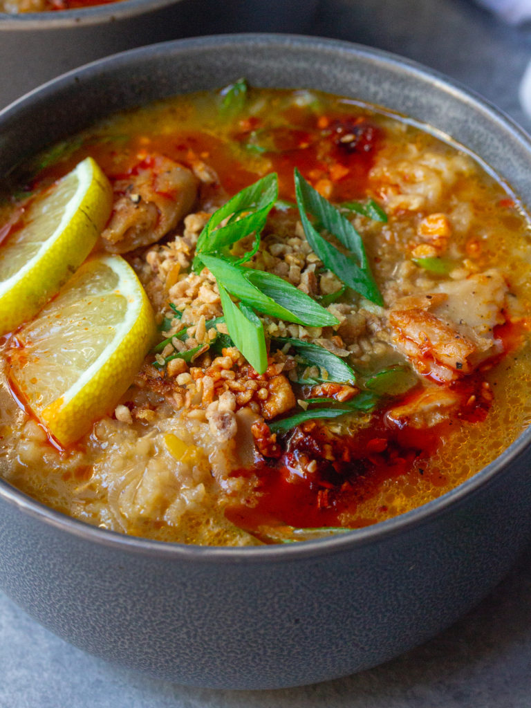 Bowl of creamy and comforting vegan arroz caldo garnished with chili oil, fried garlic, green onions, and lemon wedges.