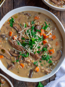 Bowl of creamy vegan wild rice and mushroom soup garnished with fresh parsley and vegan parmesan cheese.