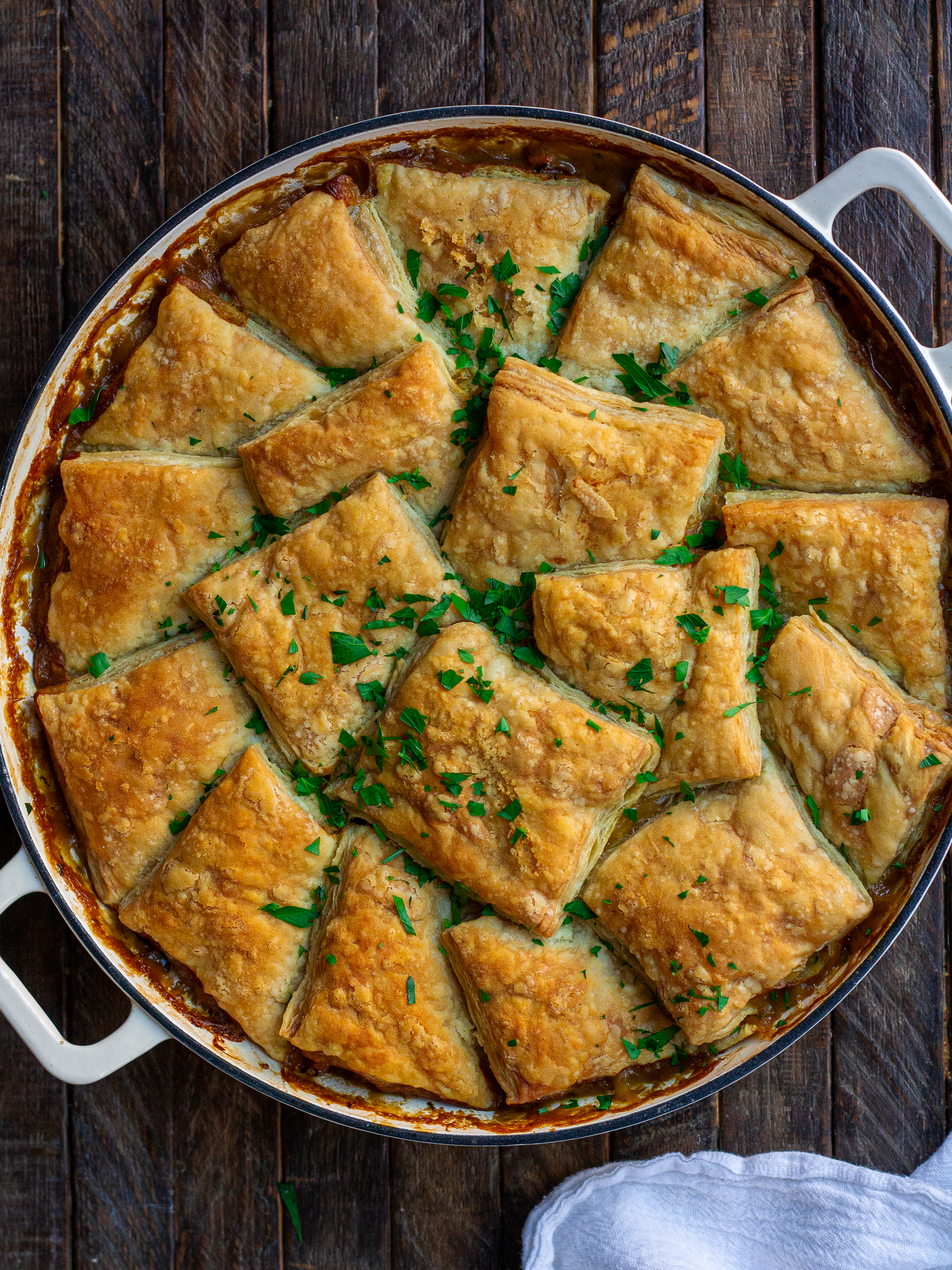 Golden-brown vegan mushroom pot pie with a flaky puff pastry crust, topped with fresh parsley.