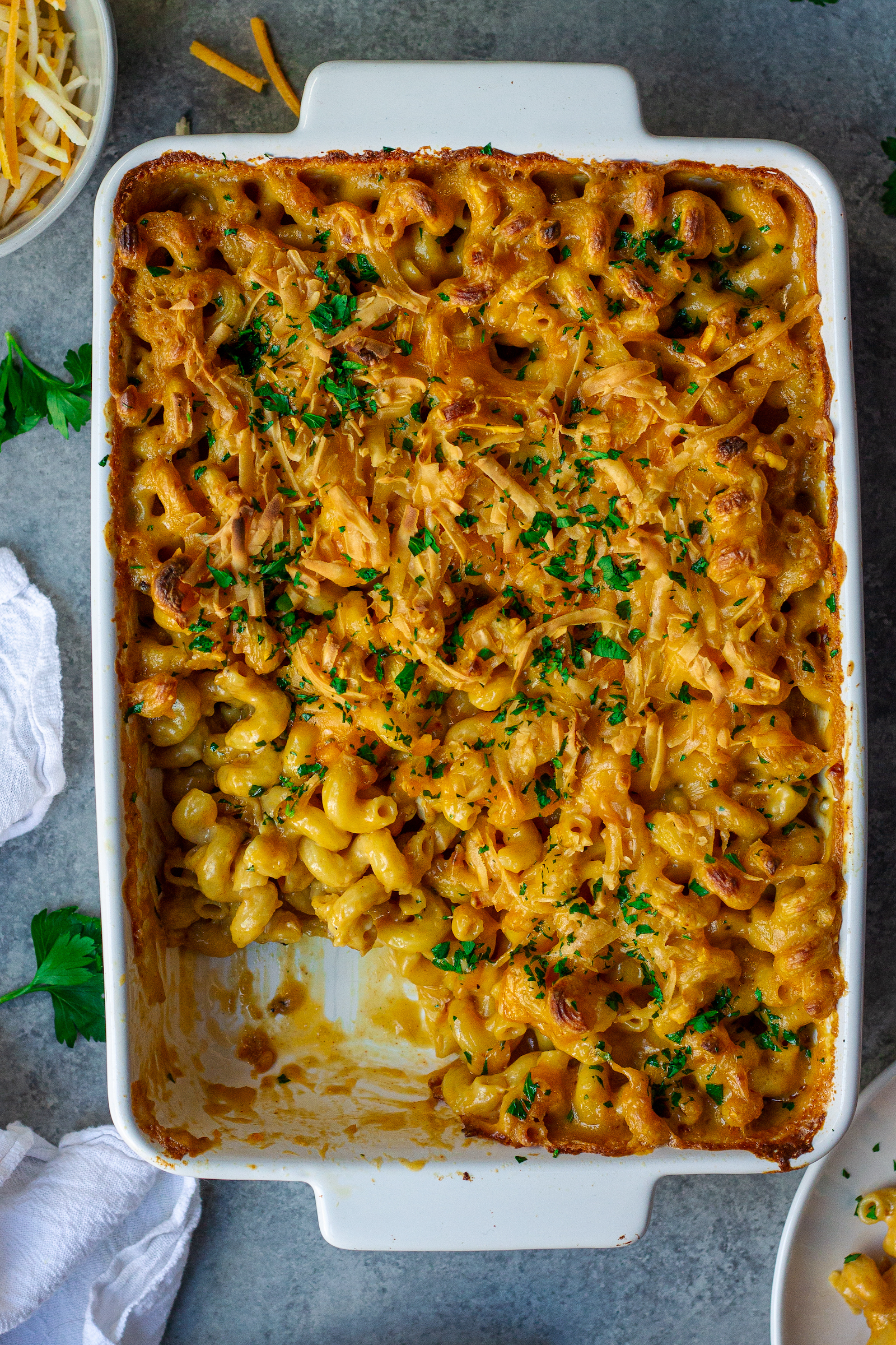Golden-brown baked vegan mac and cheese in a casserole dish with a sprinkle of fresh parsley garnish.