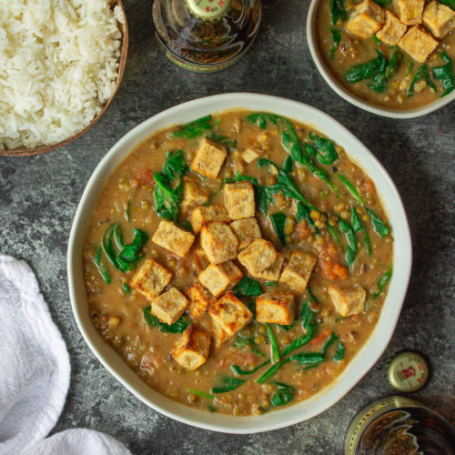 A bowl of creamy Ginisang Munggo stew topped with crispy tofu, served with a side of white rice.