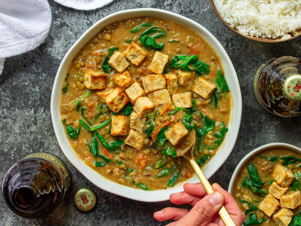 A bowl of creamy Ginisang Munggo stew topped with crispy tofu, served with a side of white rice.