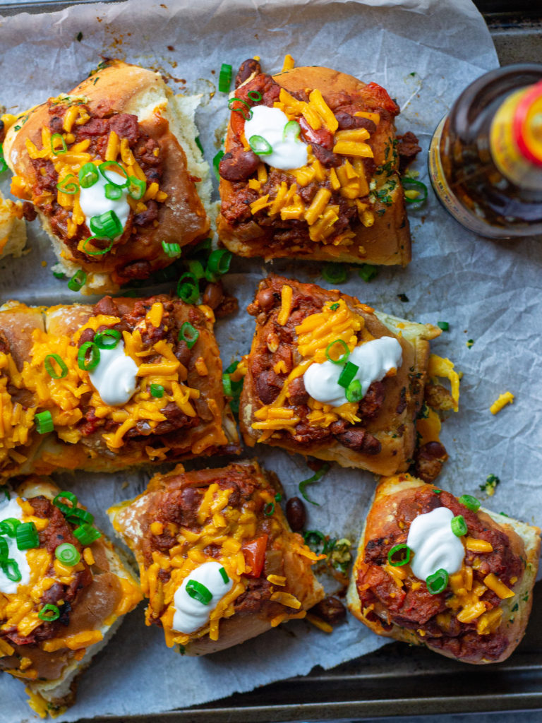 A plate of mini chili cheese dogs served with a side of extra chili.