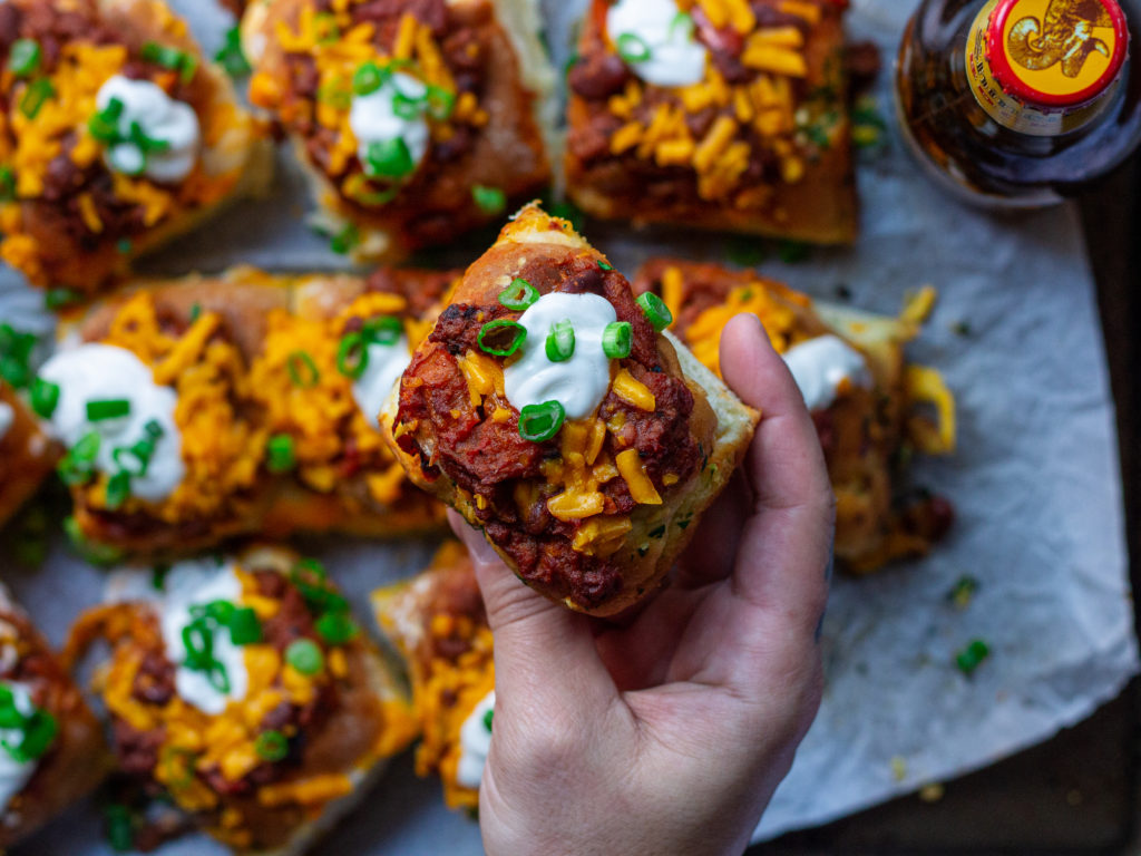 A plate of mini chili cheese dogs served with a side of extra chili.