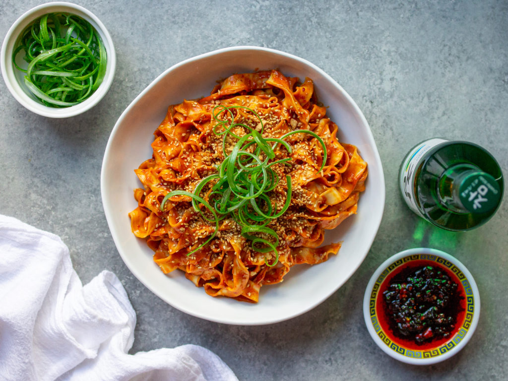A bowl of peanut gochujang noodles topped with green onions and sesame seeds.