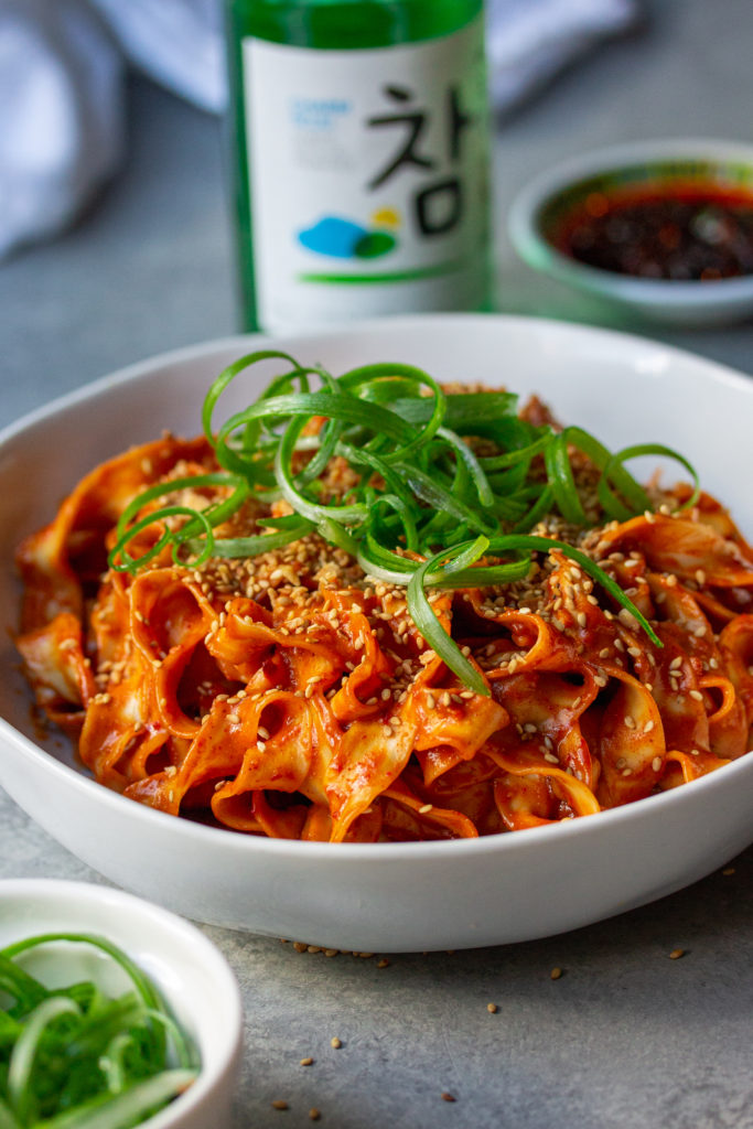 A bowl of peanut gochujang noodles topped with green onions and sesame seeds.