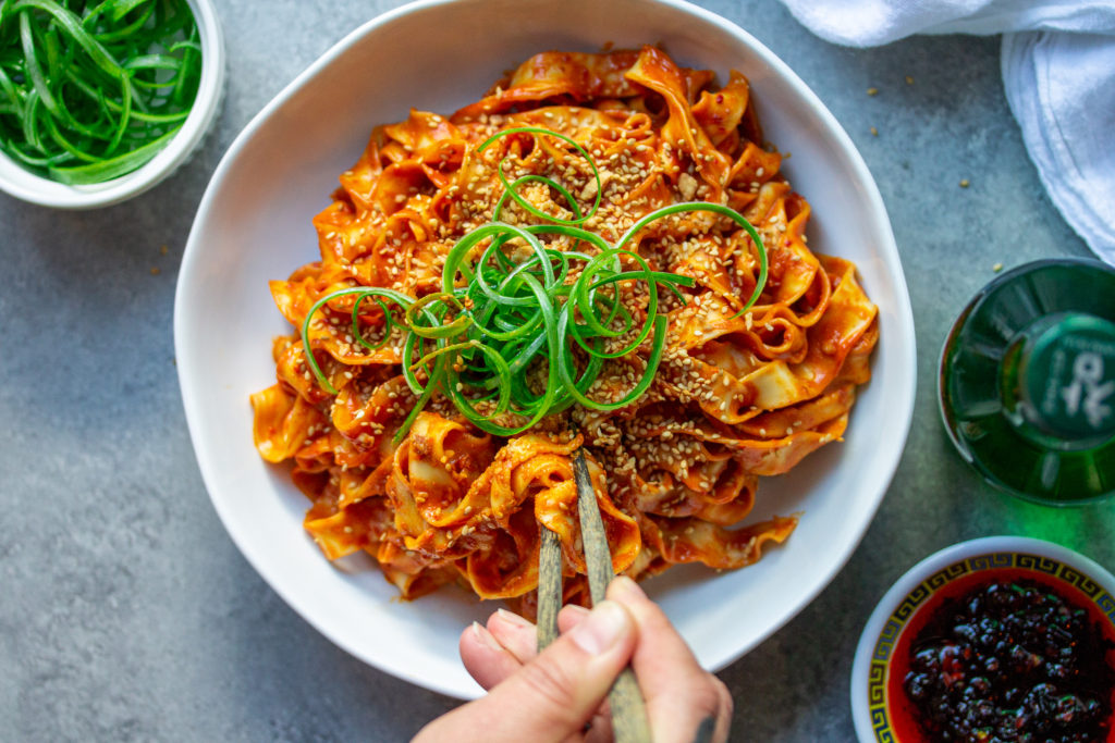 A bowl of peanut gochujang noodles topped with green onions and sesame seeds.