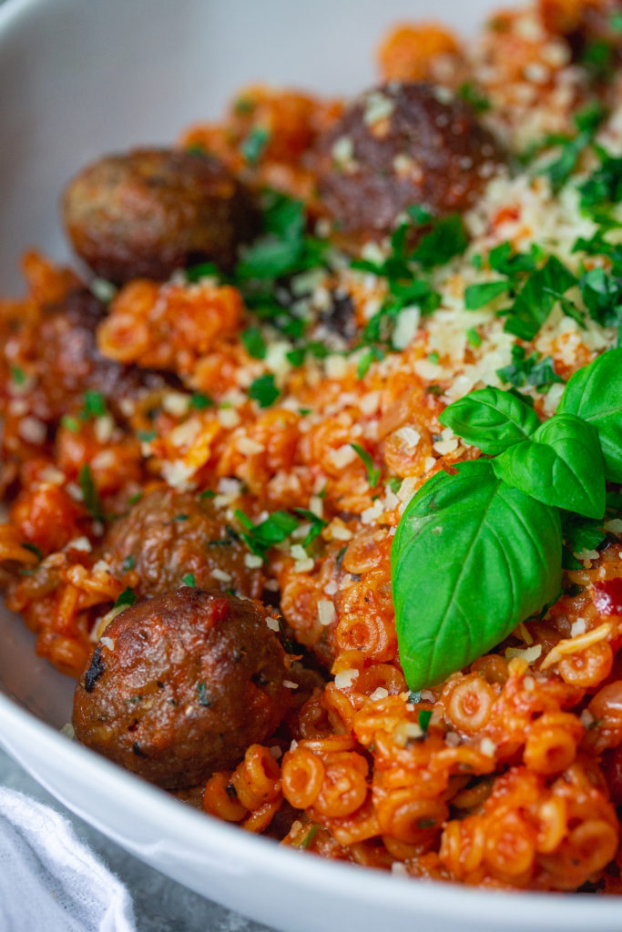 Image of the finished spaghettiOs with mini meatballs - "A bowl of homemade spaghettiOs with mini meatballs, garnished with vegan parmesan shreds and fresh parsley."