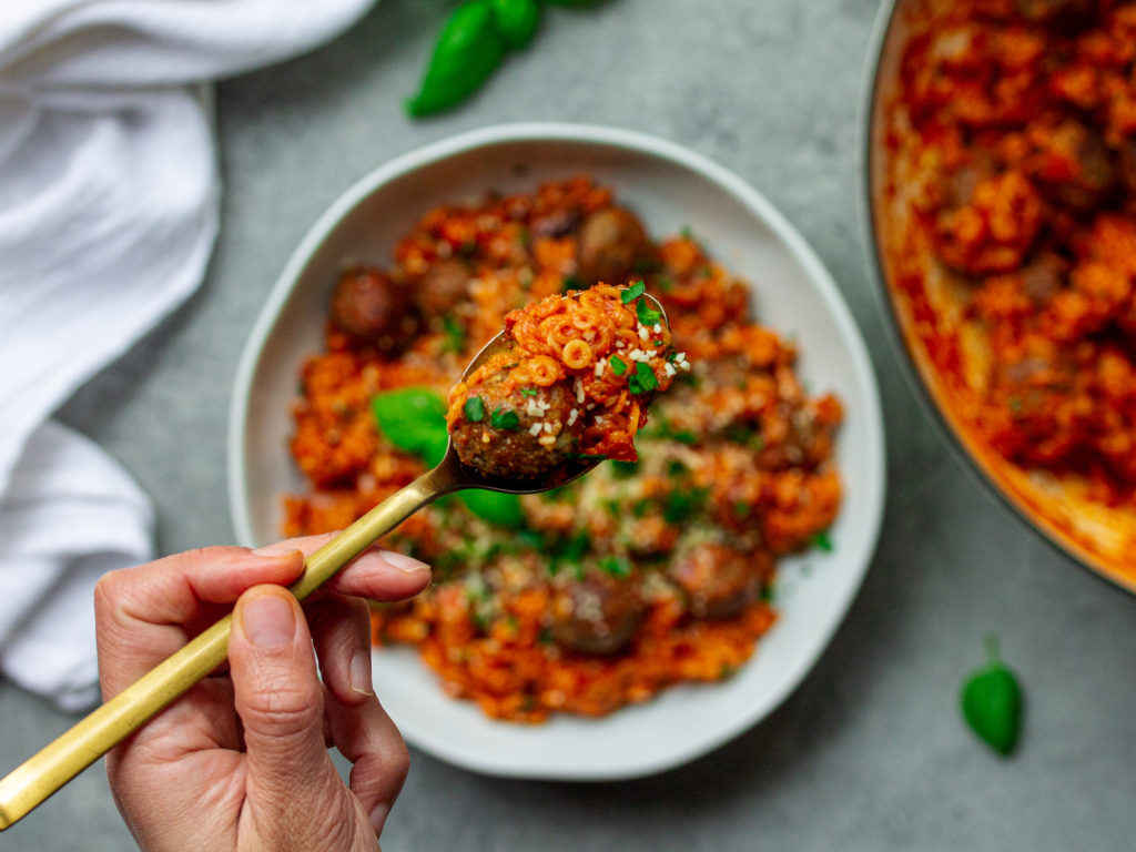 Image of the finished spaghettiOs with mini meatballs - "A bowl of homemade spaghettiOs with mini meatballs, garnished with vegan parmesan shreds and fresh parsley."