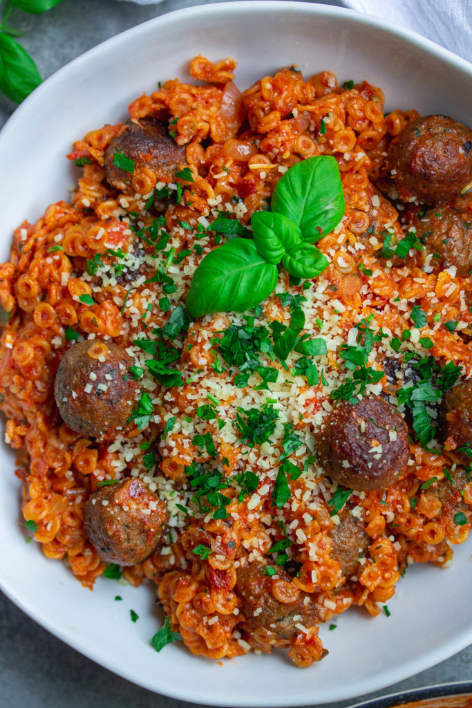 Image of the finished spaghettiOs with mini meatballs - "A bowl of homemade spaghettiOs with mini meatballs, garnished with vegan parmesan shreds and fresh parsley."