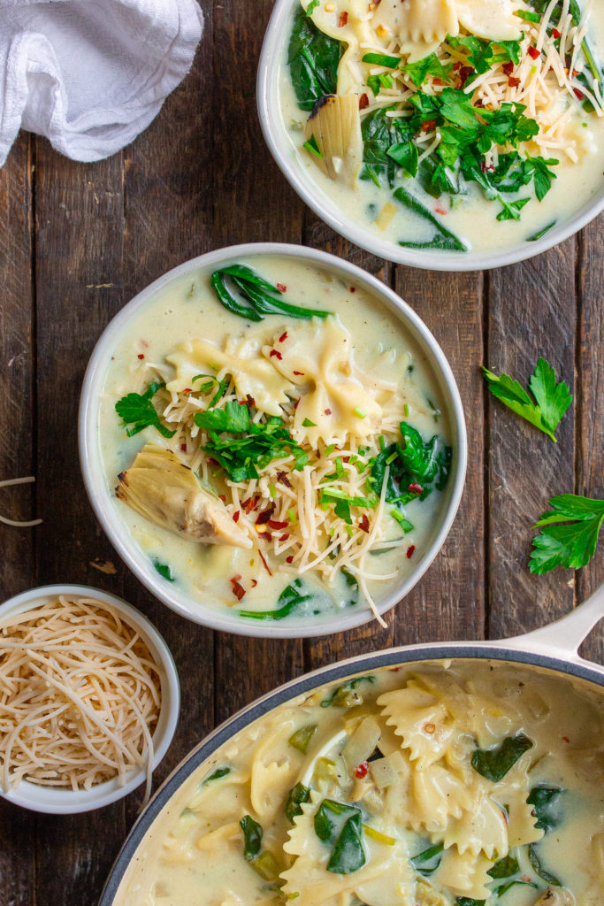 A pot of creamy soup with noodles, spinach, and artichoke hearts 